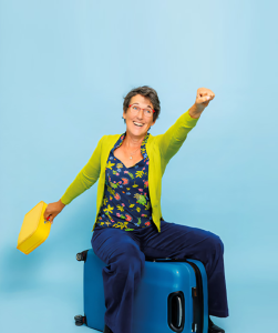 Vrouw zit blij op koffer en maakt een vlieg gebaar