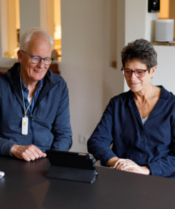 Oudere man en vrouw zitten aan tafel en kijken naar tablet op tafel