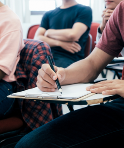 persoon schrijft met pen op papier in klaslokaal