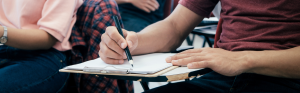 persoon schrijft met pen op papier in klaslokaal