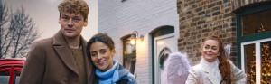 Een koppel kijkt blij, een vrouw verkleed als engel kijkt naar koppel