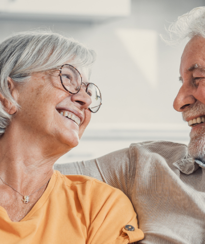 Oudere man en vrouw kijken elkaar blij aan op de bank