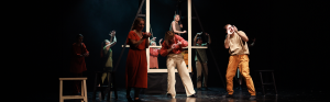 Groep mannen en vrouwen staan op podium en maken gebaren en spelen een theaterstuk