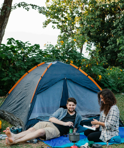 Blije man en vrouw zitten voor tent op de camping